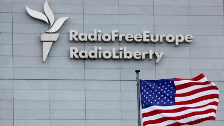 A flag of the United States flies in-front of a sign of Radio Free Europe/Radio Liberty at its headquarters in Prague, Czech Republic, March 17, 2025.